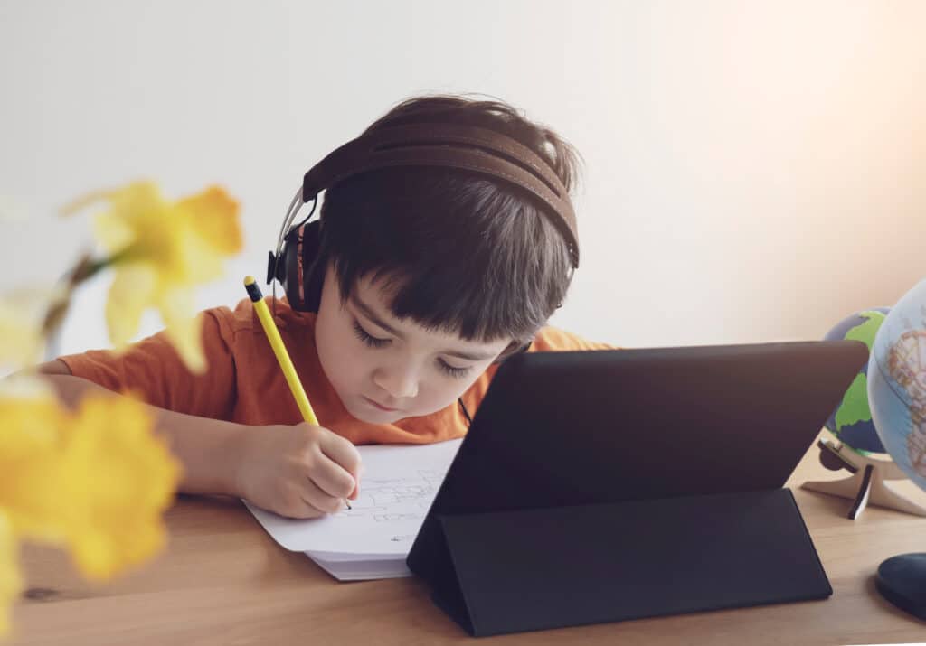 Child with Headphones Does Learning Exercise with Tablet and Paper