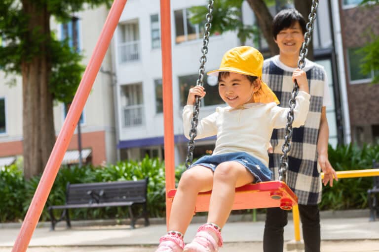 Image of a Nanny Playing with a Child on playground Swingset