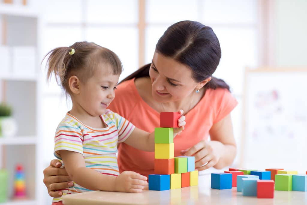 A Nanny and a Toddler Play with Mutli-Color Building Blocks