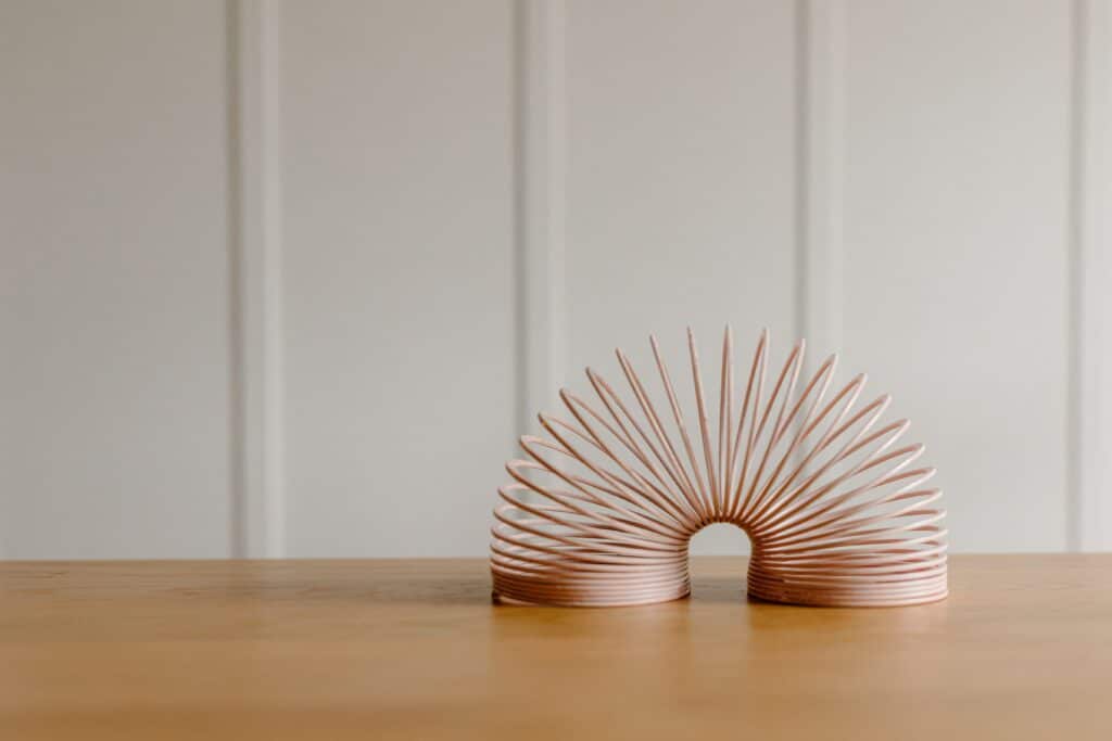A pink slinky sits on a table, bent in half to represent flexibility