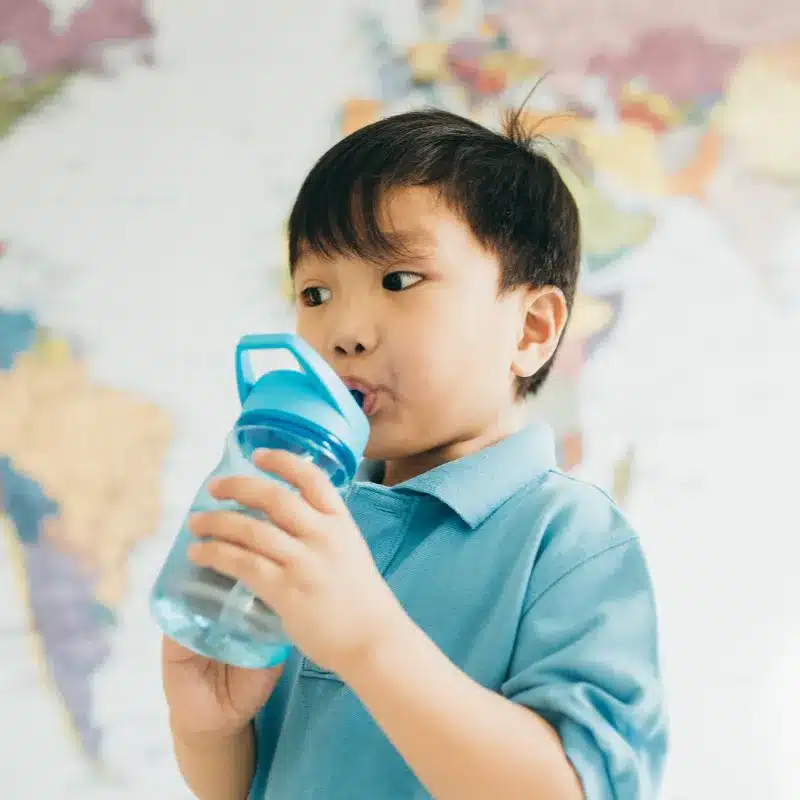A kid drinking water in a sippy cup