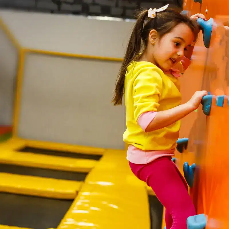 A little girl climbing in a wall inside an indoor play space