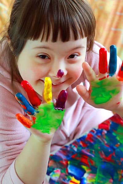 a girl with Down syndrome showing colorful hands while painting